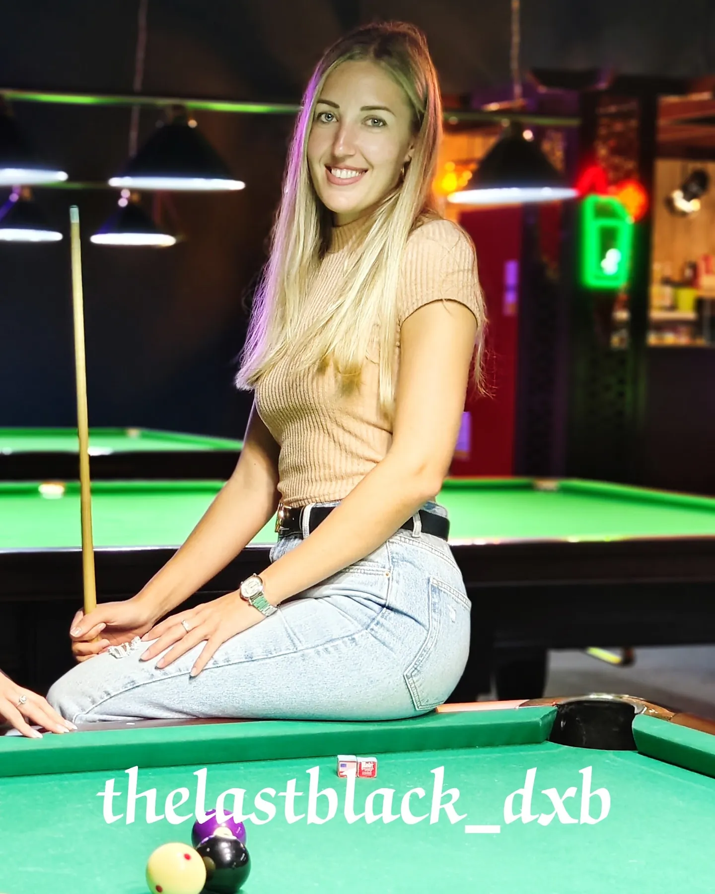 Player seated on a pool table with a cue